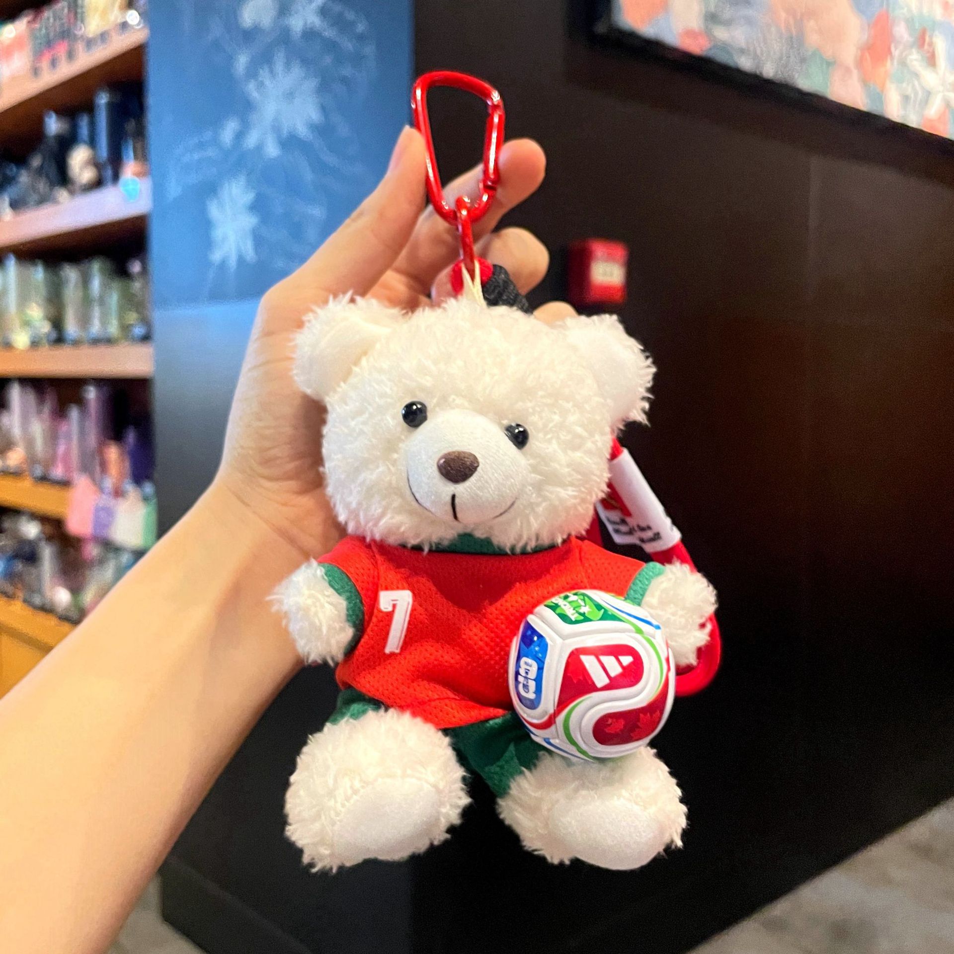 Plush bear keychain in red kit holding a world ball